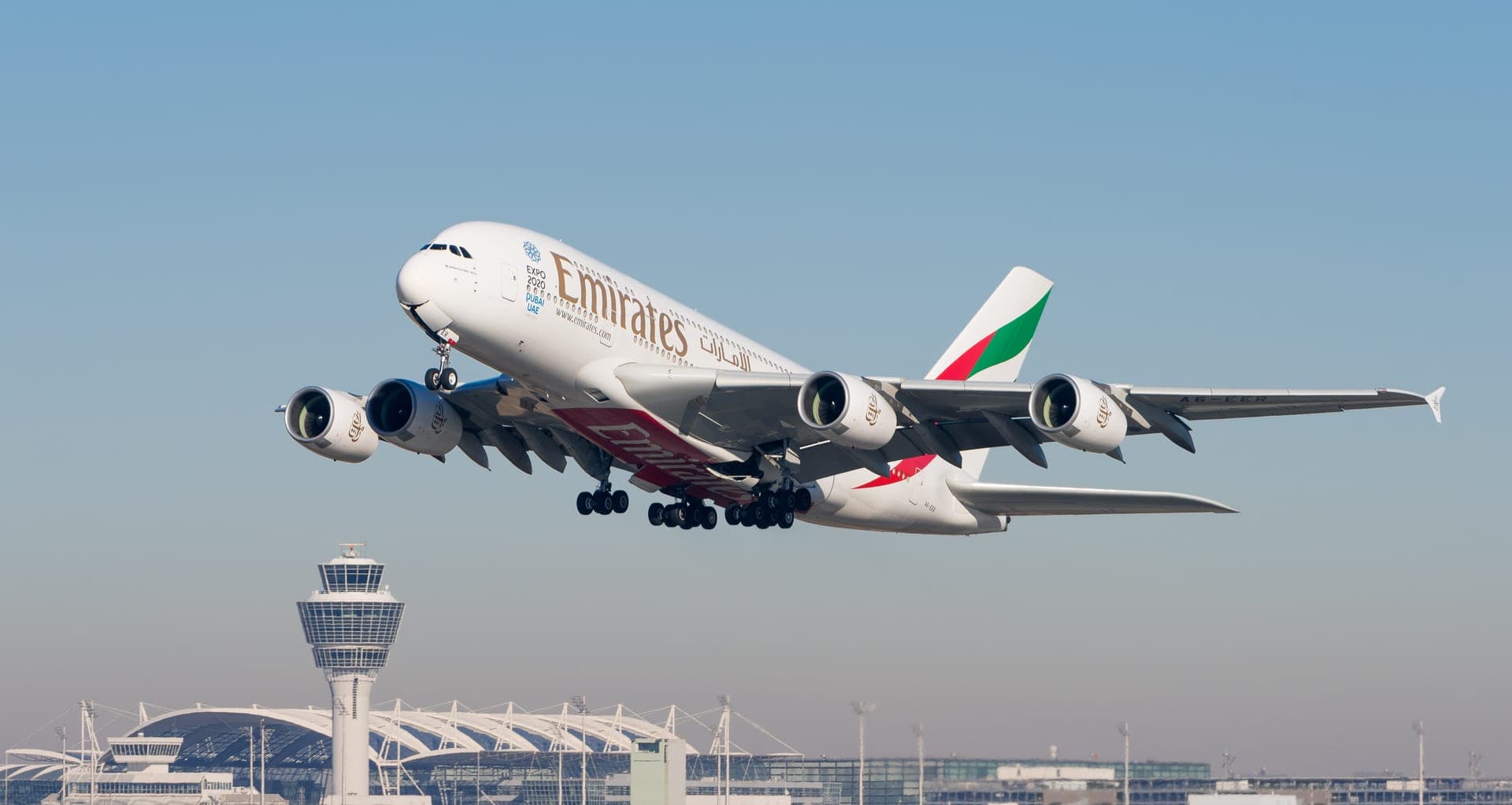 Un Airbus A380-861 d'Emirates en montée après son décollage de l'aéroport de Munich, les quatre moteurs visibles sous le fuselage à double pont sur toute sa longueur