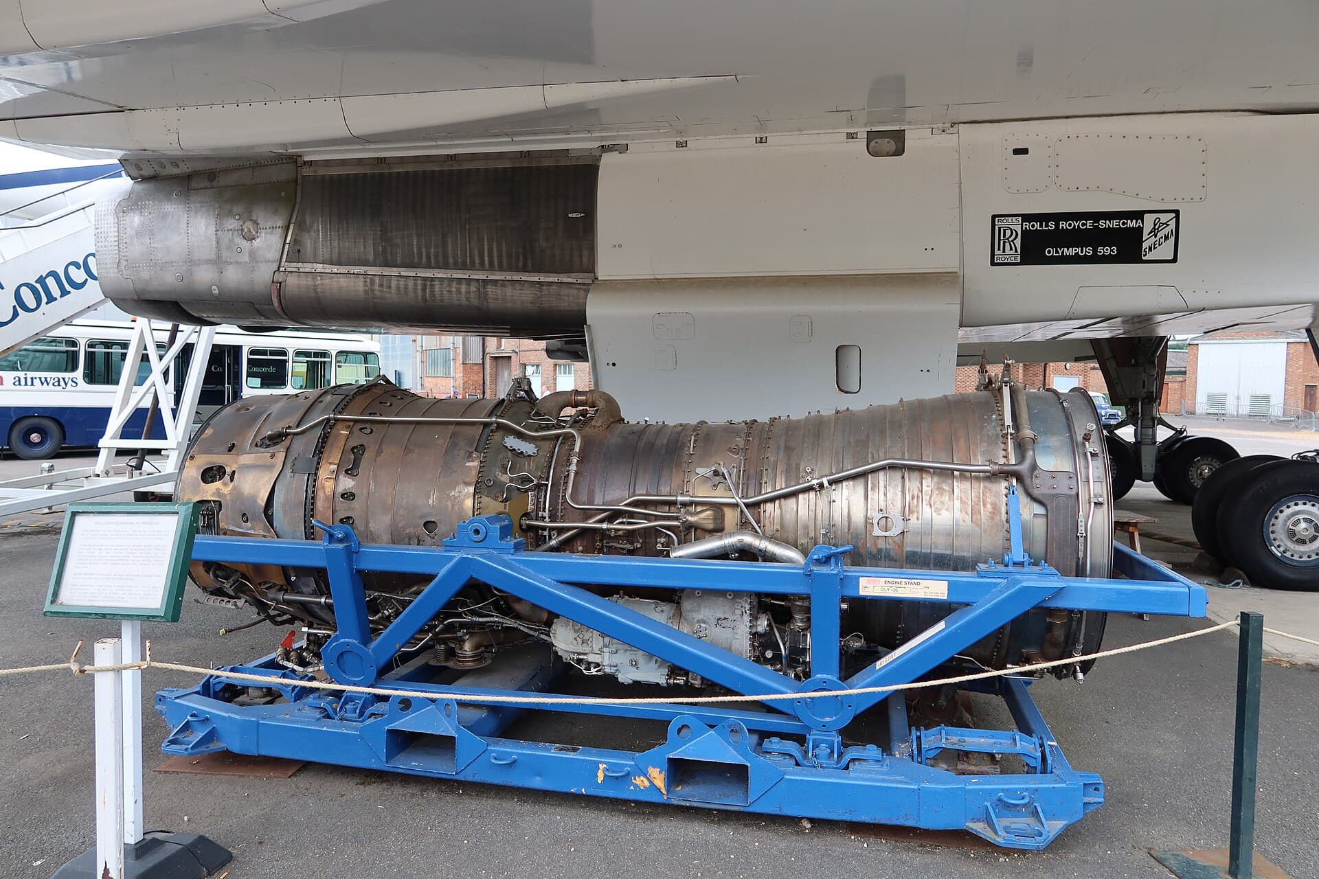 A Rolls-Royce/SNECMA Olympus 593 on its engine stand at Brooklands Museum, beneath the wing of a Concorde whose nacelle carries the engine's maker's plate