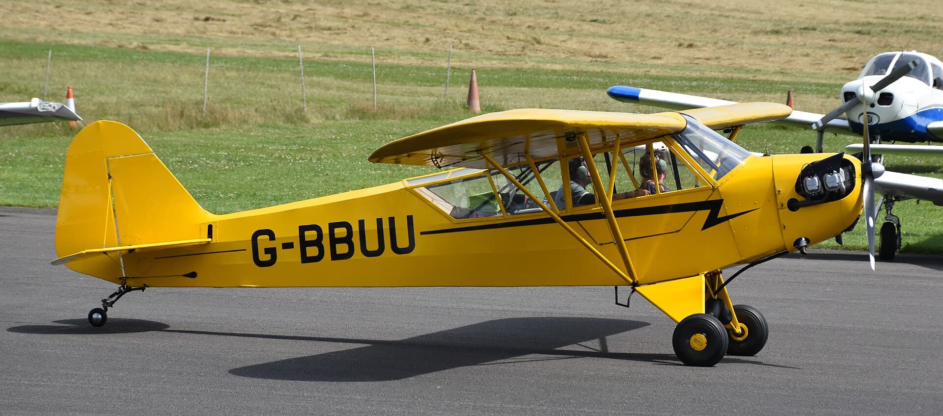 Un Piper J-3 Cub jaune, immatriculé G-BBUU, stationné sur le tarmac