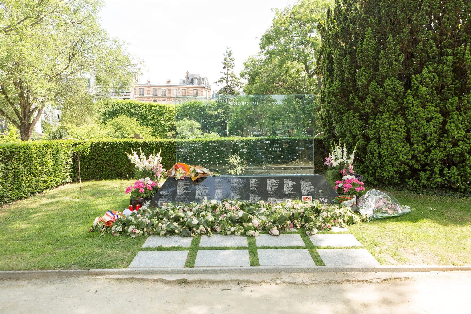 The memorial to the victims of flight AF447 at Père-Lachaise cemetery in Paris: a glass stele inscribed Rio de Janeiro to Paris, 01/06/2009, above the names of the dead, with flowers laid before it.