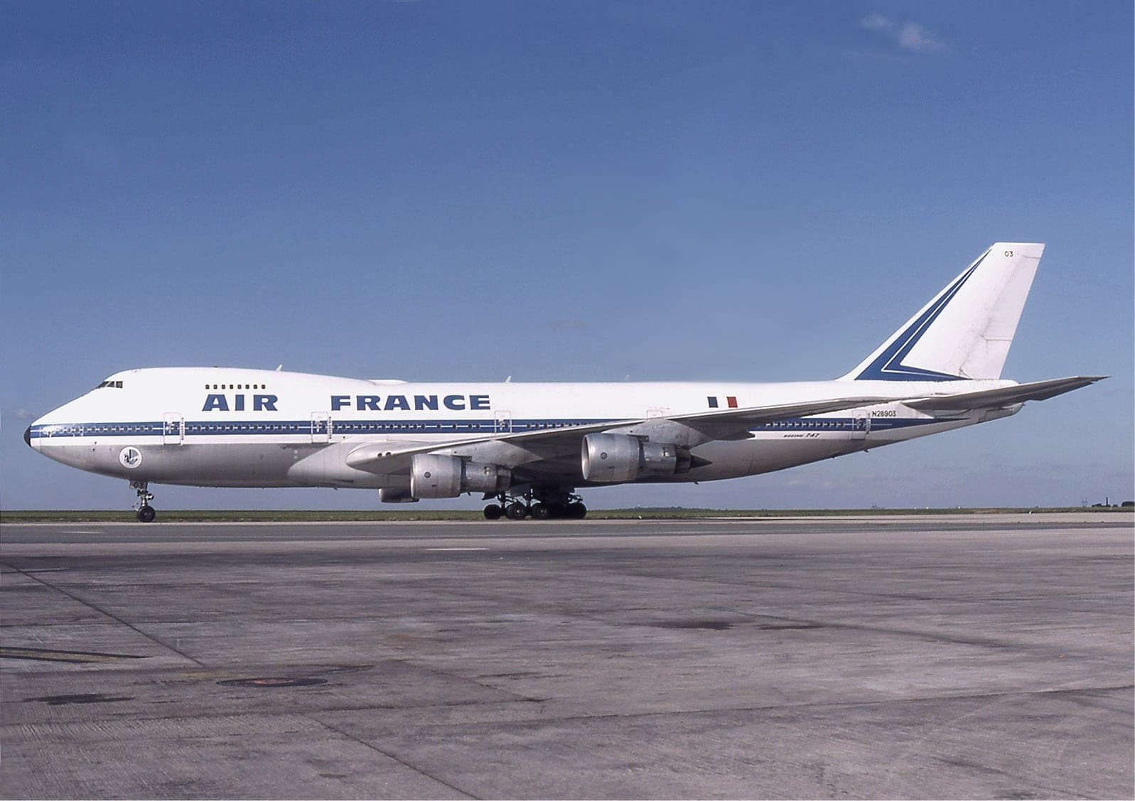 An Air France Boeing 747-100 on the apron in the pre-1976 livery: bare metal below a blue cheatline, with the twin blue stripes on the fin.