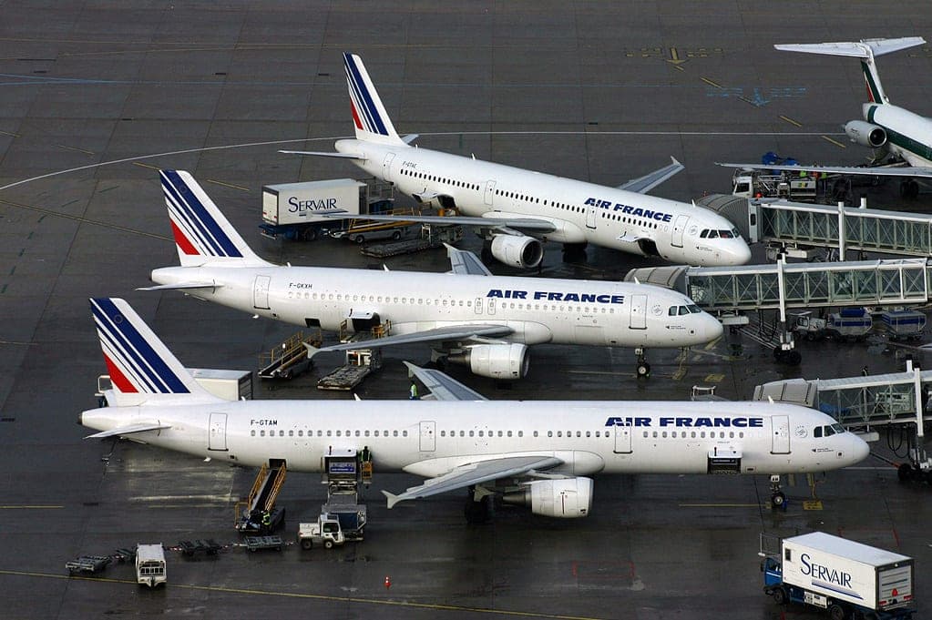 Three Air France Airbus A320-family aircraft at the gates of Terminal 2F at Paris-Charles de Gaulle, with Servair catering trucks alongside.