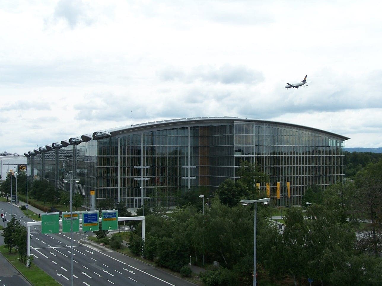 The Lufthansa Aviation Center at Frankfurt Airport, the glass-roofed office building that houses much of the airline's management, with an aircraft overhead.