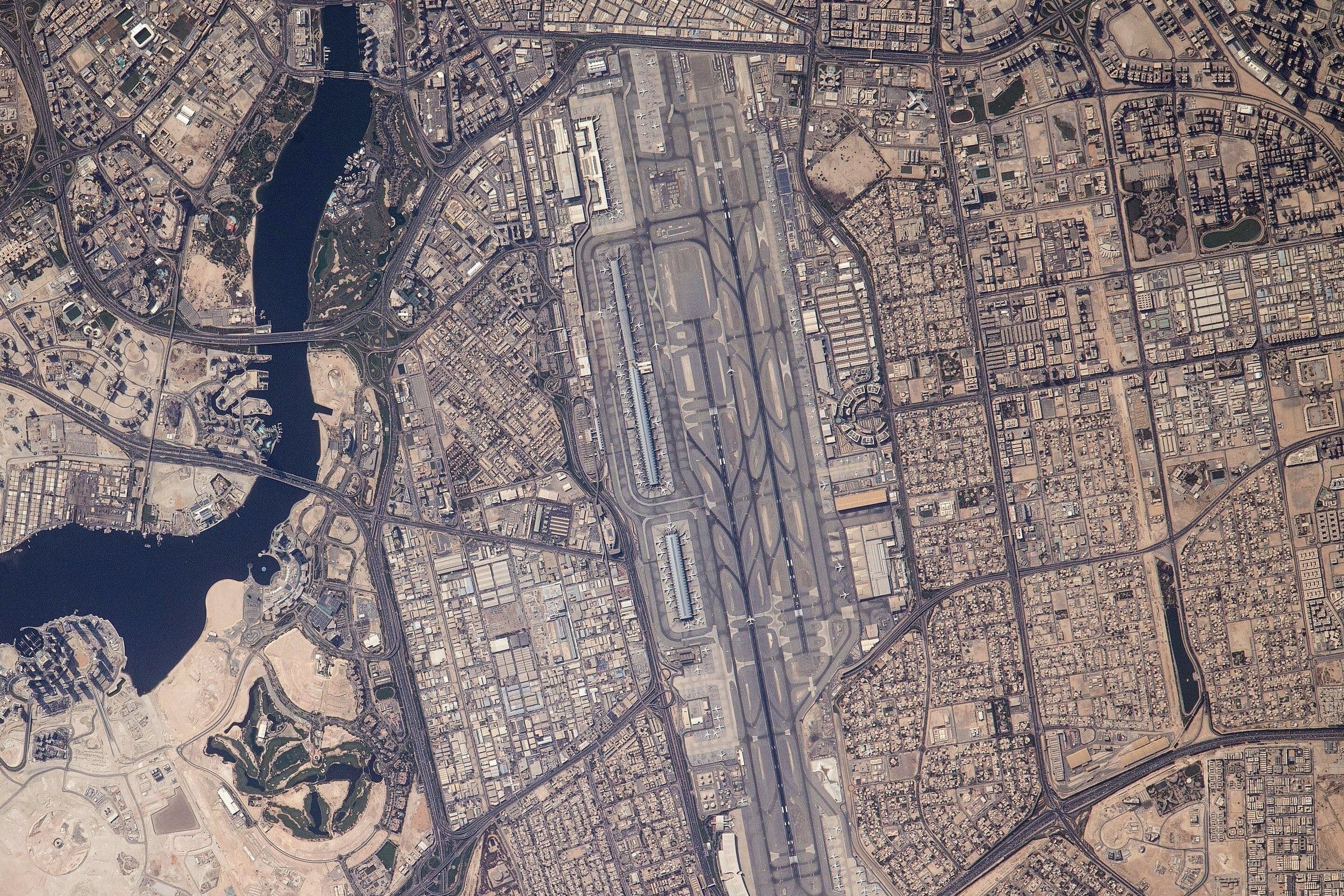 Dubaï International vu à la verticale depuis la Station spatiale internationale en mai 2021 : deux longues pistes parallèles, les aérogares le long, et la crique de Dubaï à l'ouest