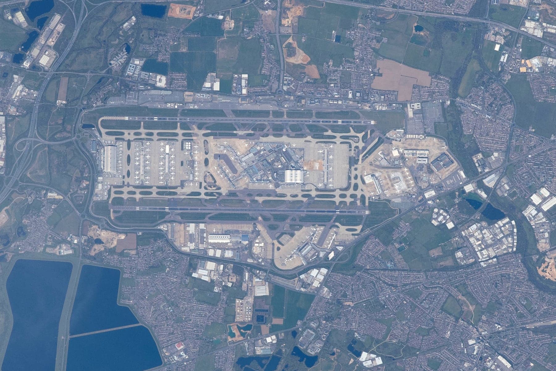Photographie verticale en couleur de Heathrow prise depuis la Station spatiale internationale en avril 2021 : les deux pistes parallèles orientées est-ouest encadrant la zone centrale des terminaux, le Terminal 5 à l'extrémité ouest, la zone de fret au sud et le Terminal 4 au sud-est, au milieu de la banlieue ouest de Londres et, à l'ouest et au sud-ouest, des réservoirs de la vallée de la Colne