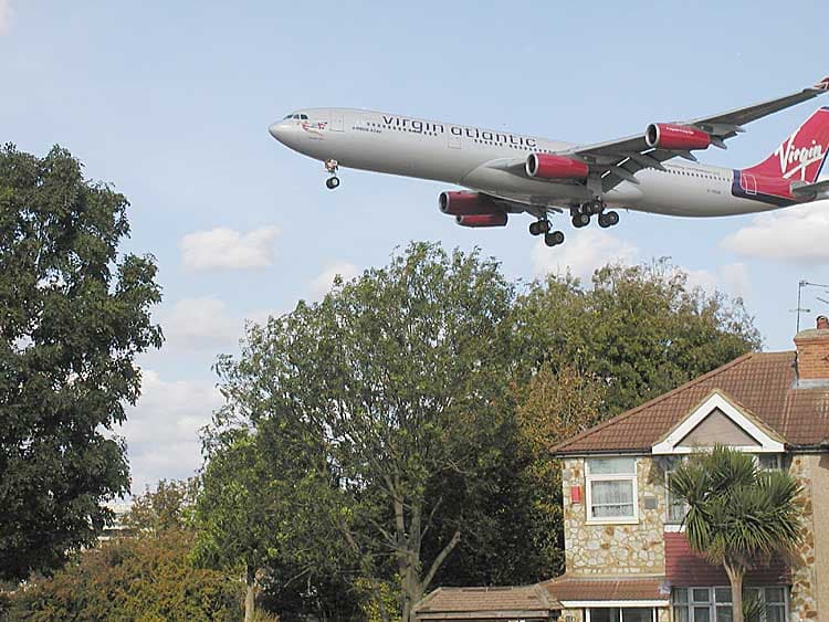 A Virgin Atlantic Airbus A340 crossing the rooftops on final approach, seen from Myrtle Avenue beside the airport's south-eastern boundary