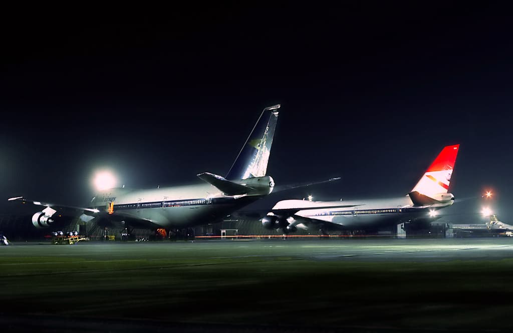 Two early Boeing 747s at Heathrow's maintenance base at night in 1977, one still wearing basic BOAC colours and the other in transitional British Airways livery