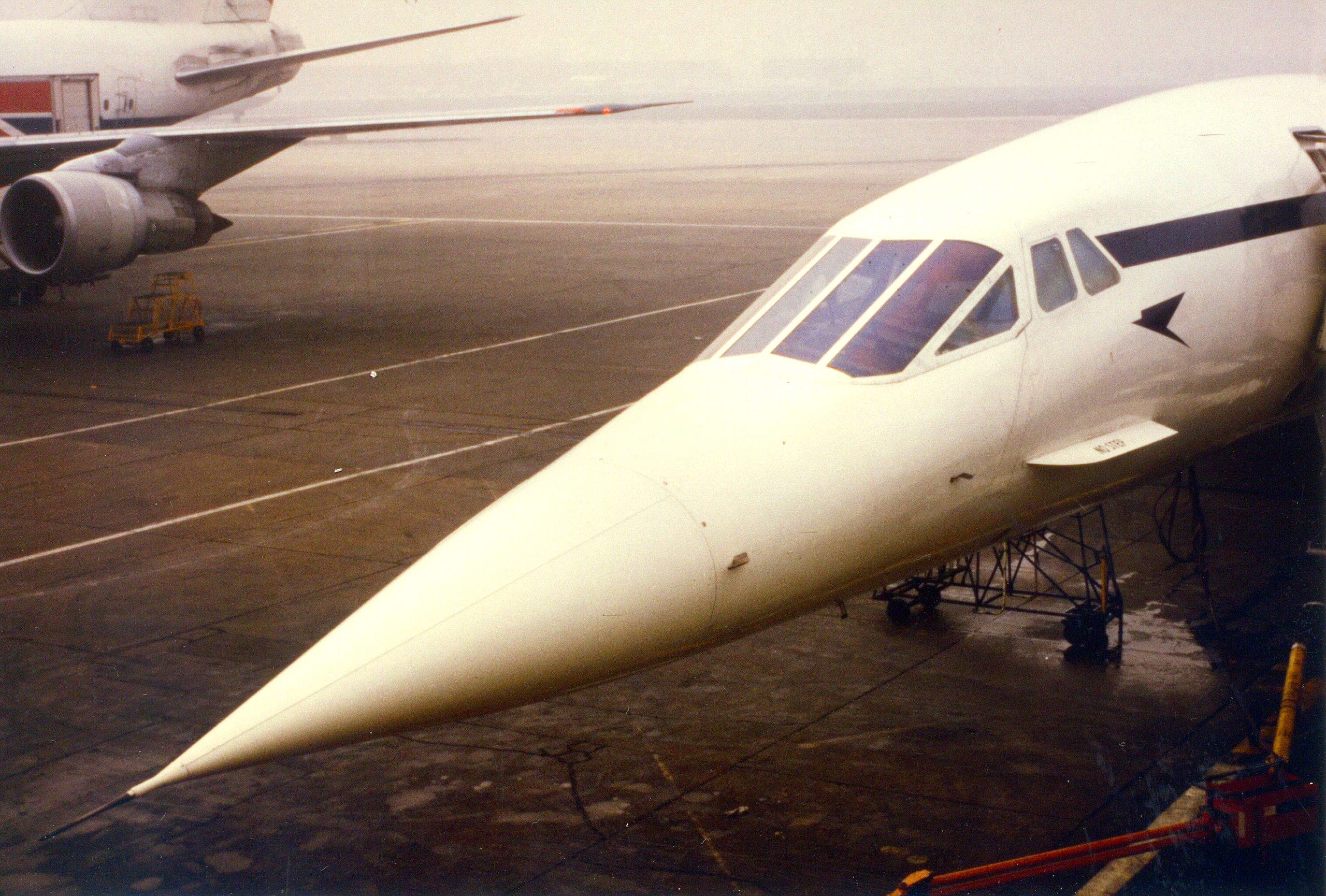 British Airways Concorde G-BOAB on a wet Heathrow stand in 1984, nose drooped, with a widebody parked behind