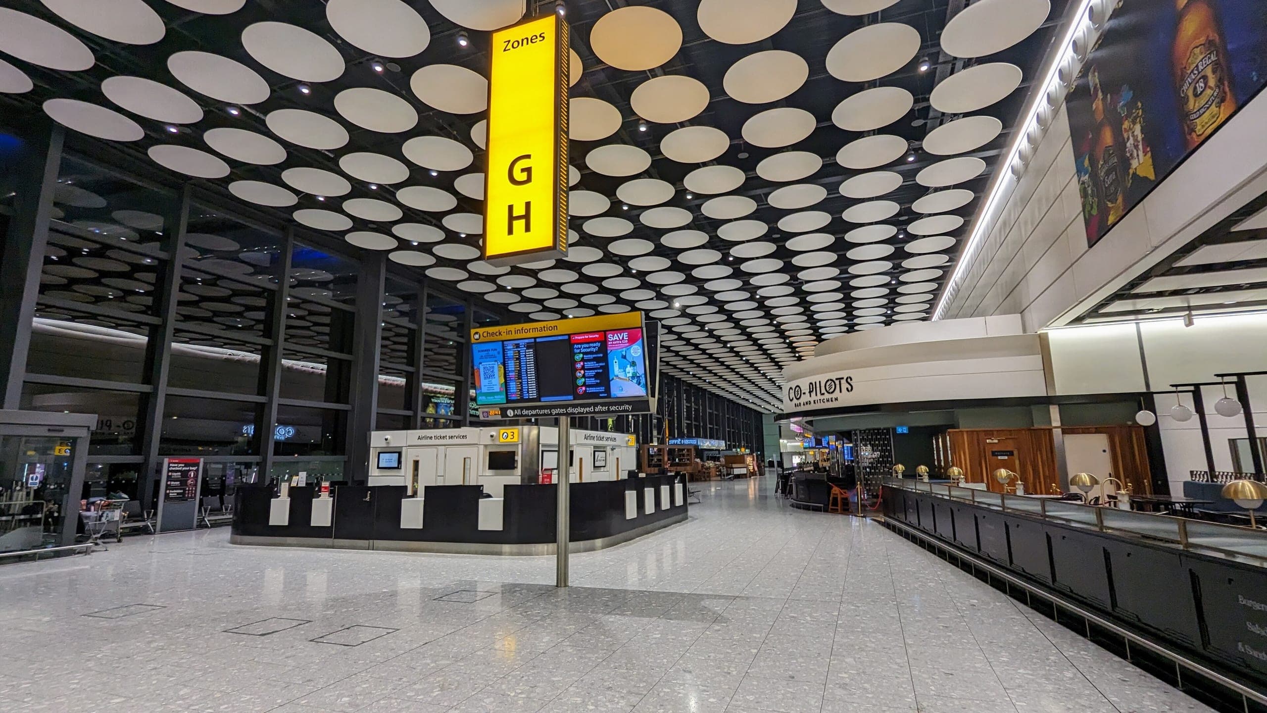 The pre-security concourse of Terminal 4 under its perforated disc ceiling, check-in zone G and H signed overhead