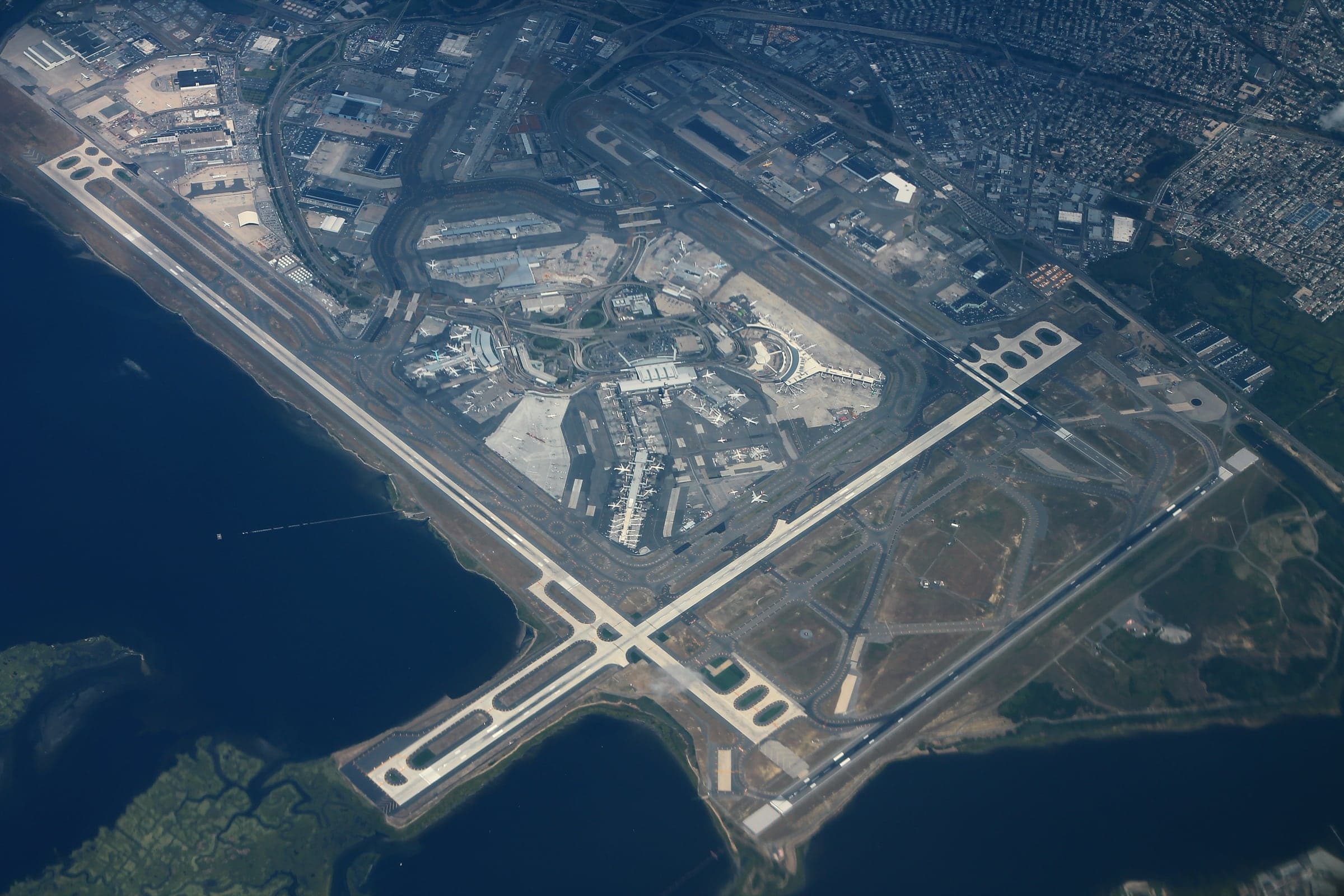 L'aéroport entier vu du ciel en 2016 : l'anneau central des aérogares dans sa boucle routière, les longues paires de pistes se croisant à angle droit, et Jamaica Bay sur trois côtés