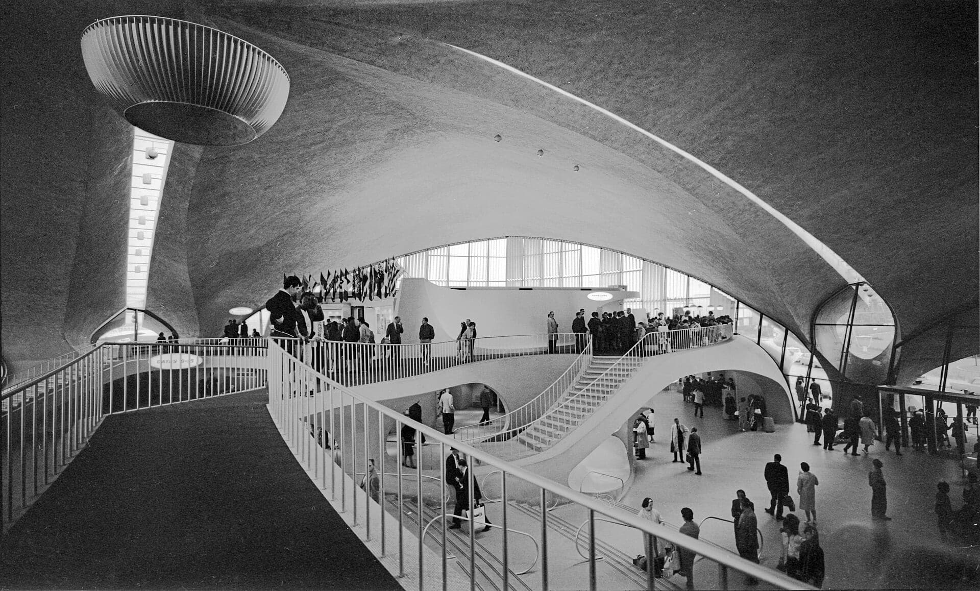 Inside the TWA Flight Center in 1963: sweeping concrete balconies and stairs under the curved shell roof, passengers crossing the main hall