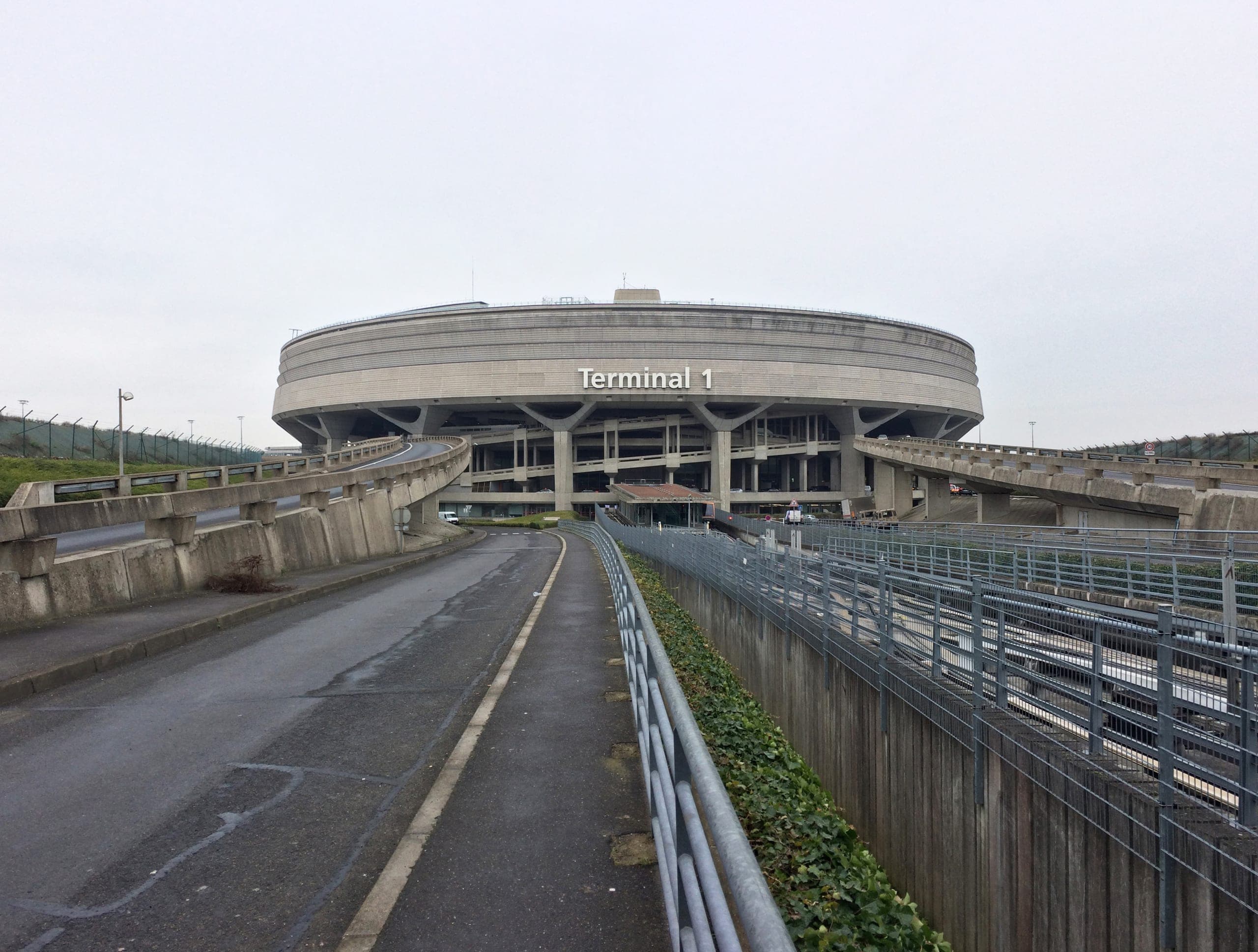 Terminal 1 seen from its access ramp, the drum raised on splayed concrete legs above the roadway