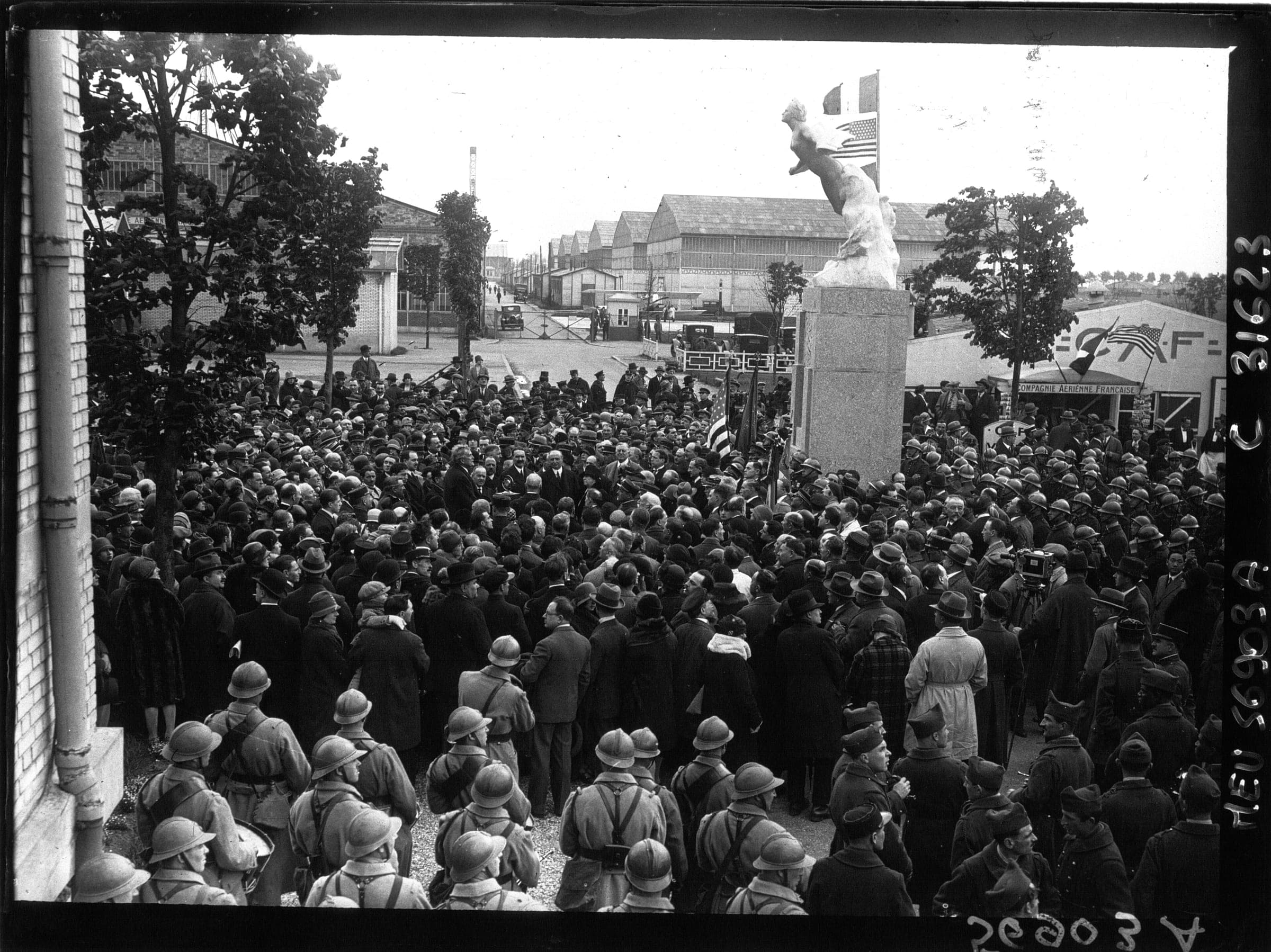 Crowds and soldiers at the unveiling of the monument to Nungesser, Coli and Lindbergh at Le Bourget, with the old hangars behind