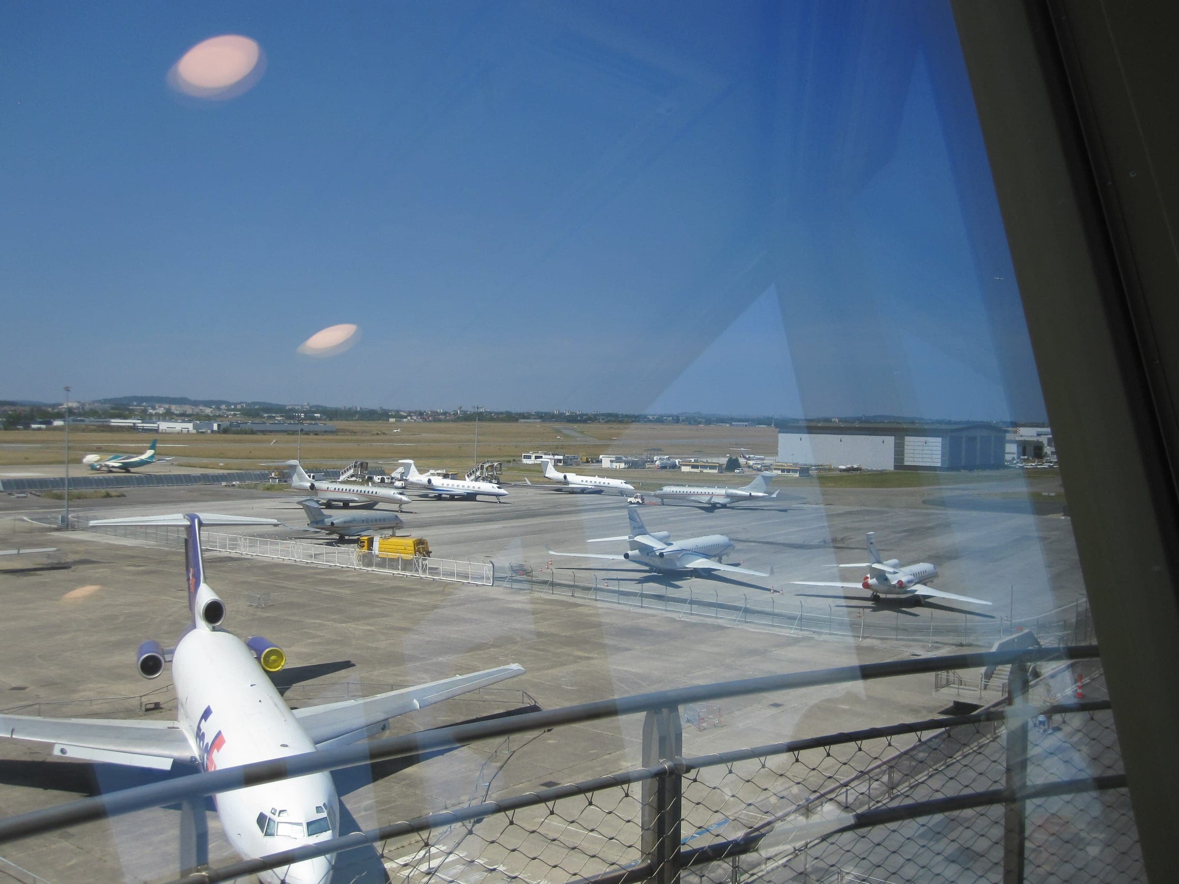 Business jets on the apron seen through the glass of the old control tower, the tail of a museum airliner in the foreground