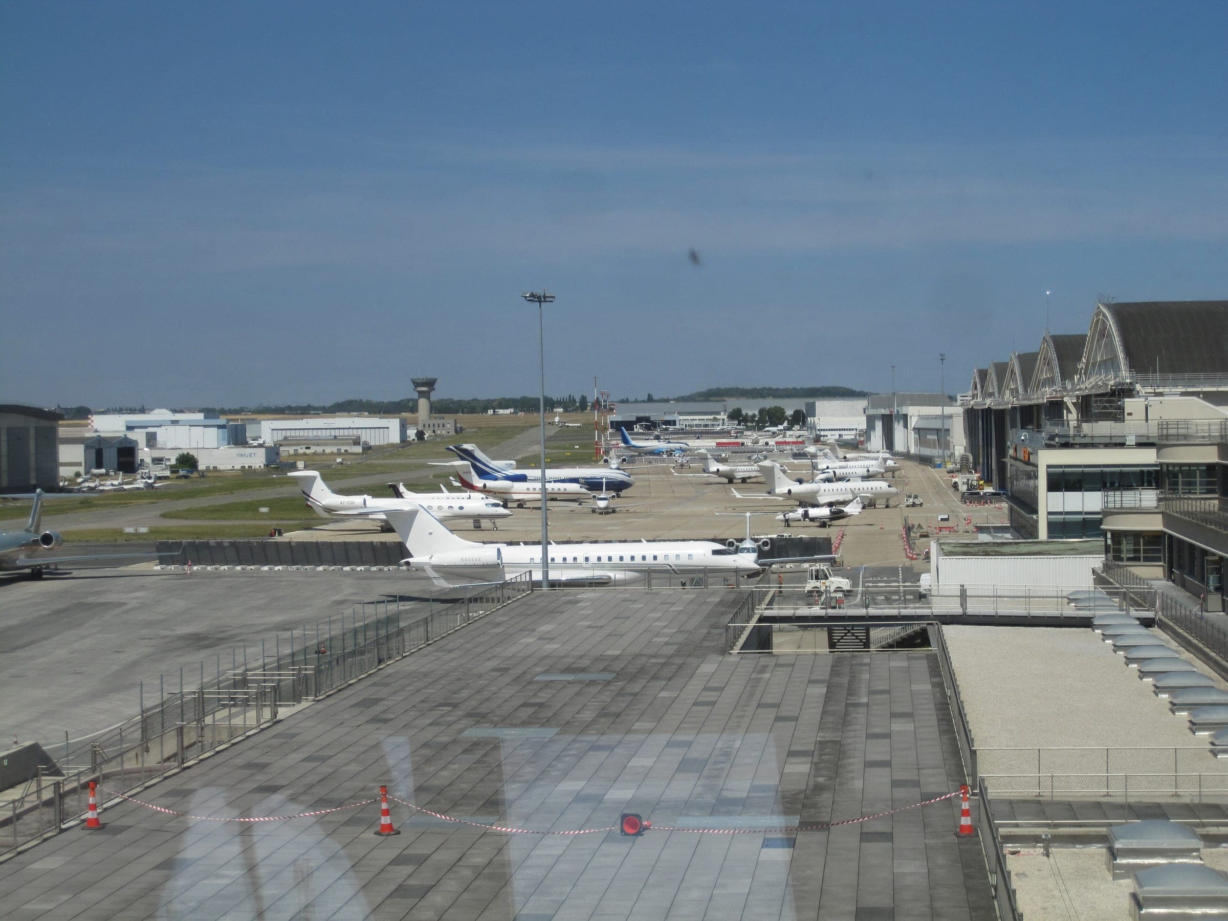Business jets parked on the apron seen from the terminal's viewing terrace, with the modern control tower and hangars beyond