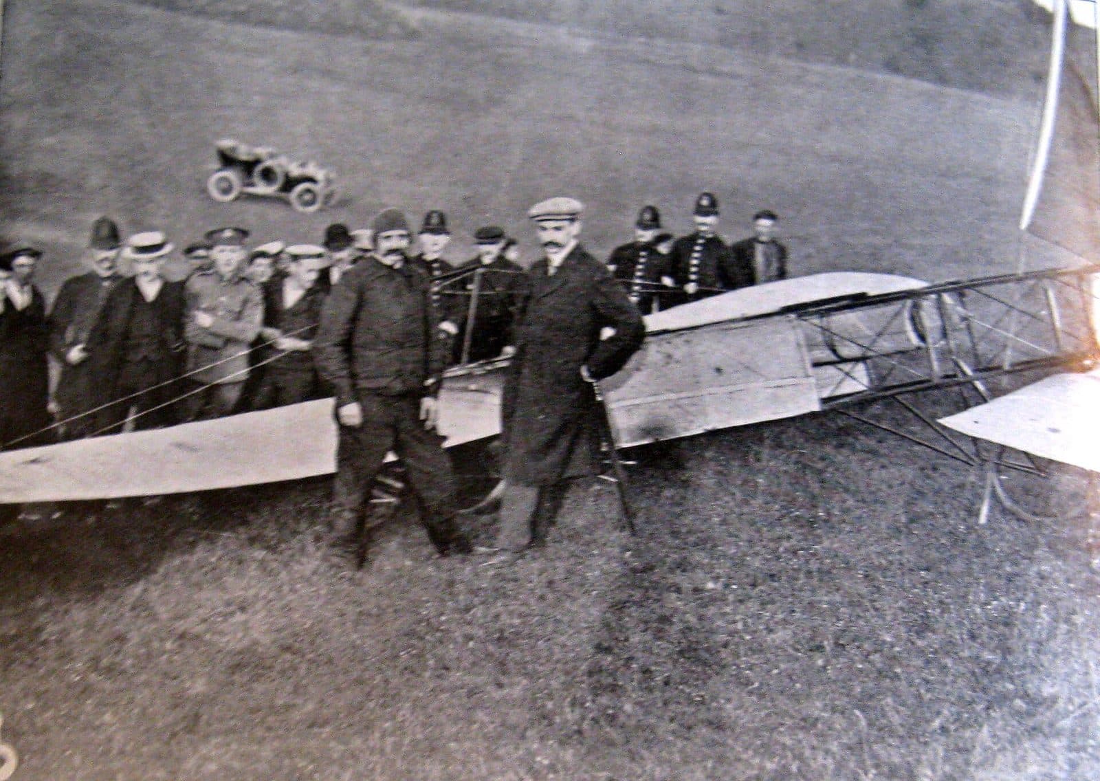 Blériot debout parmi des policiers et des spectateurs, à côté de son monoplan endommagé, dans la prairie de Douvres.