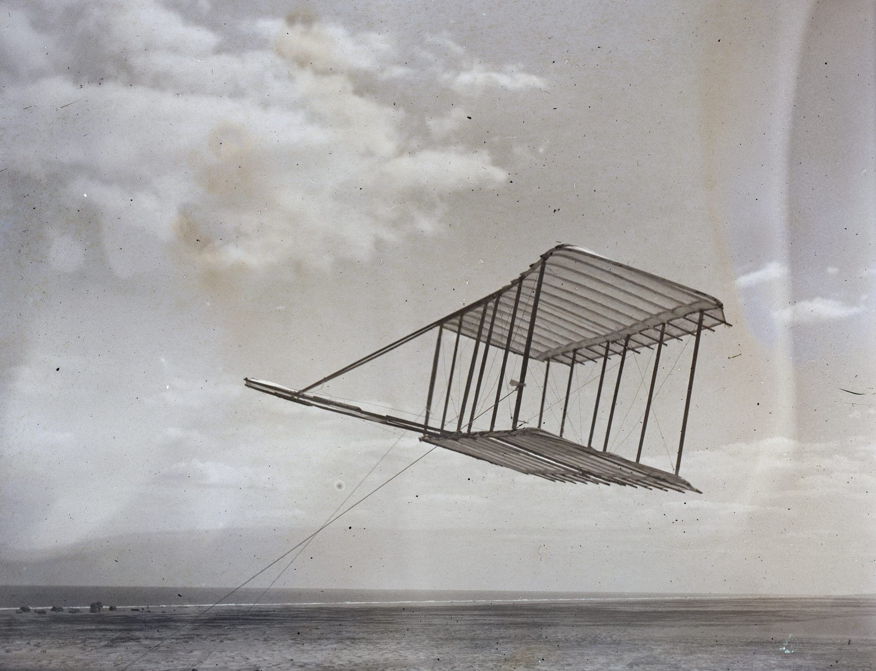 Le planeur de 1900 volant en cerf-volant au bout de ses câbles au-dessus du sable de Kitty Hawk, sa gouverne de profondeur avant bien visible.