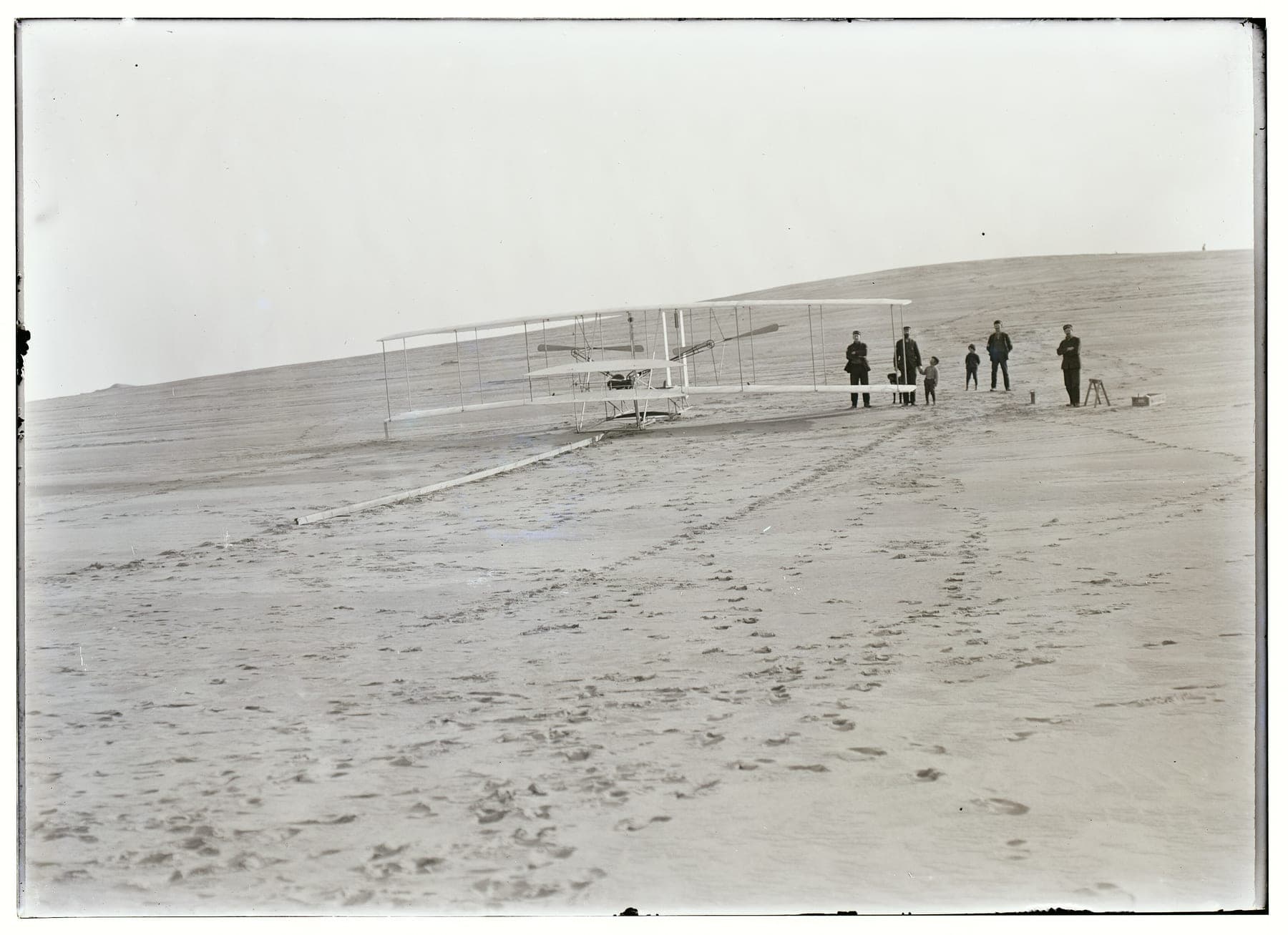 Le Flyer sur son rail de lancement au pied de la grande dune, le 14 décembre 1903, quatre hommes de la station de sauvetage à ses côtés.