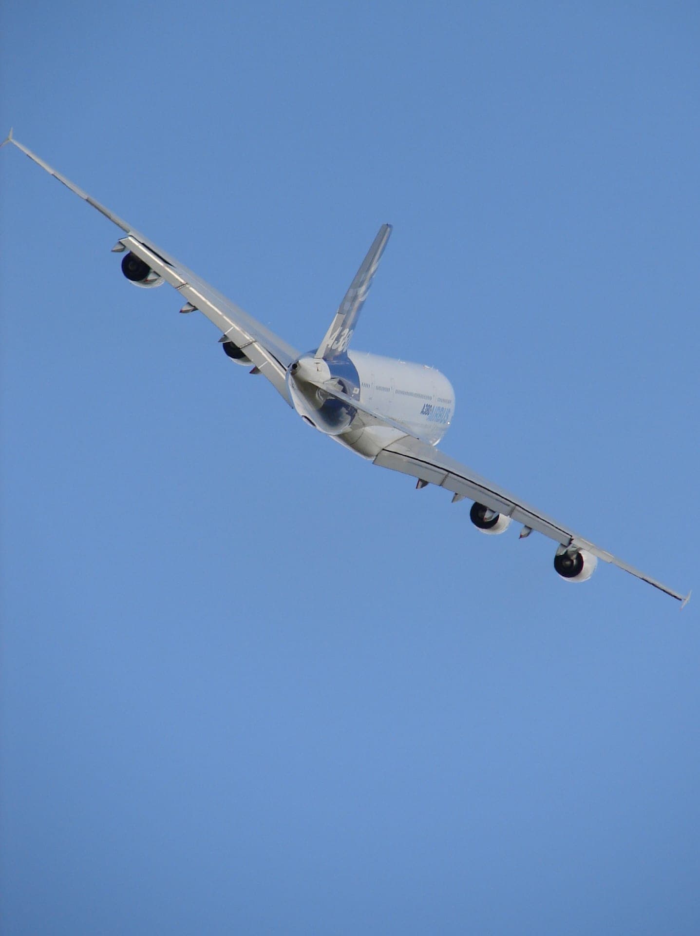Un Airbus A380 en virage serré, son immense voilure et ses quatre moteurs vus par en dessous, se détachant sur le ciel