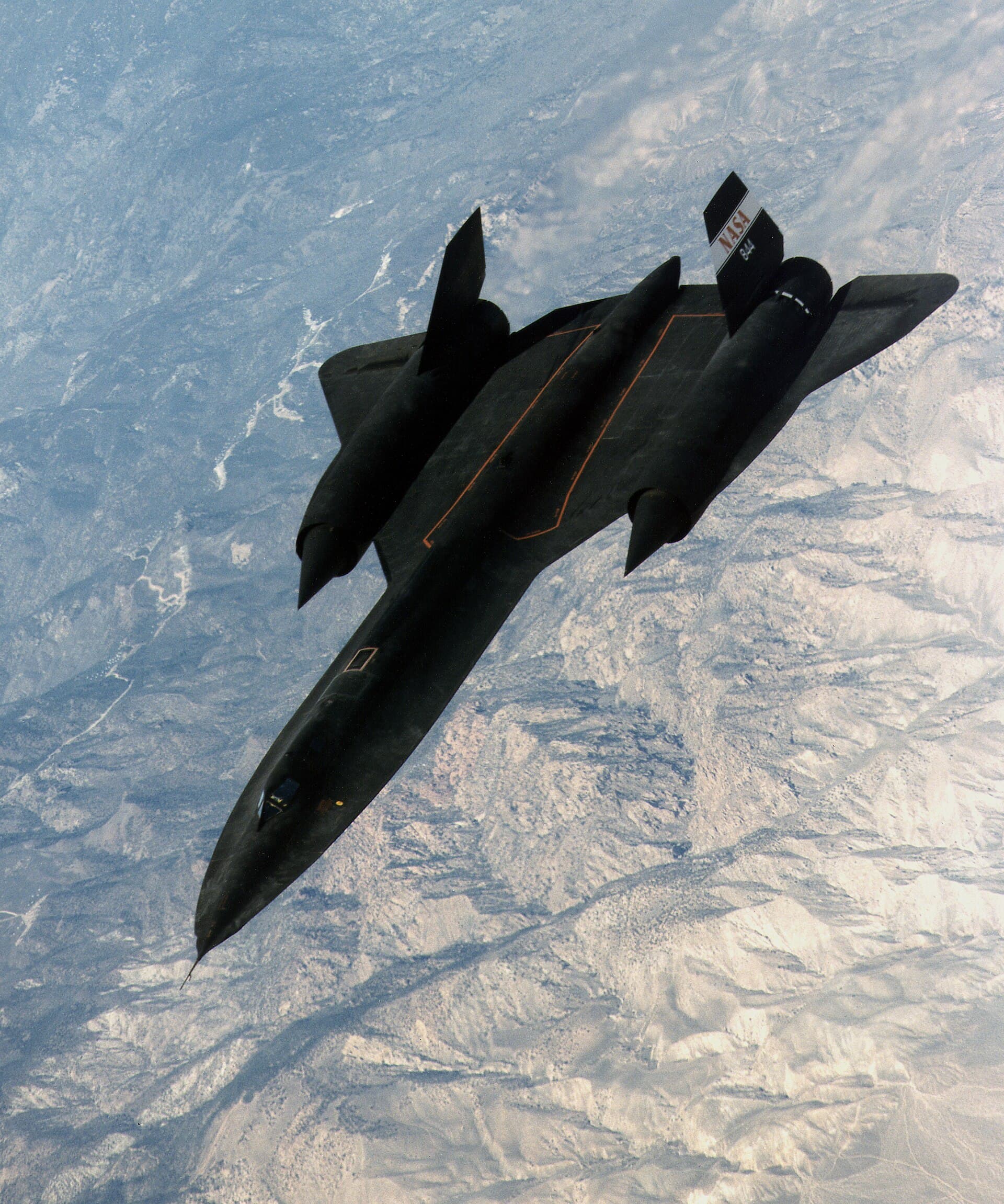 NASA's SR-71A banking hard over snow-capped mountains, underside and engine nacelles fully exposed to the camera