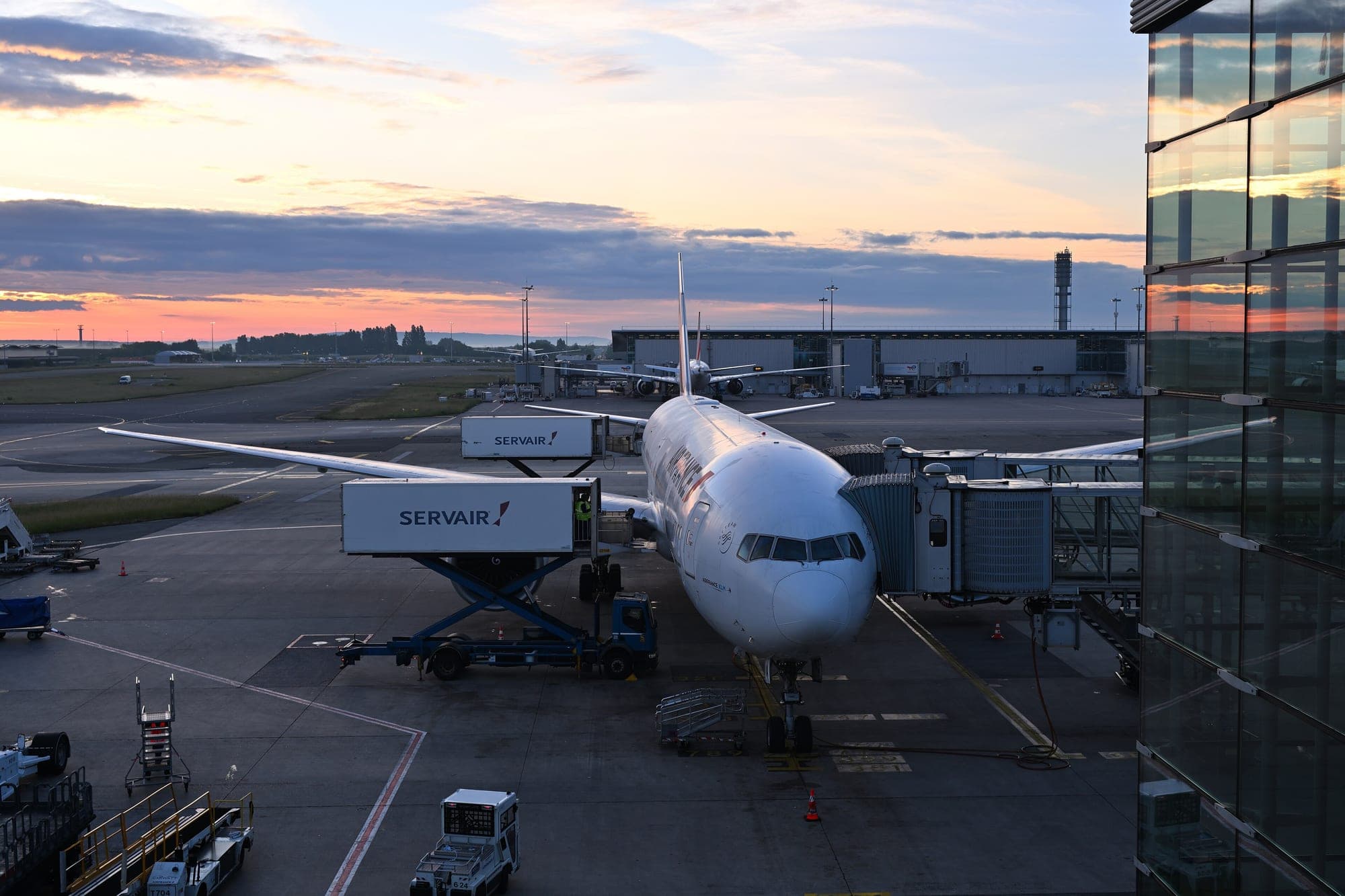 An Air France Boeing 777-300ER at its stand at Paris-Charles de Gaulle at dawn, jet bridge and catering trucks in place.